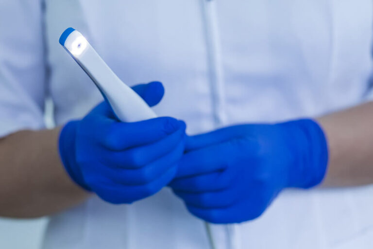A dental professional wearing a white scrub and blue gloves holding an intra oral camera while the lights on.