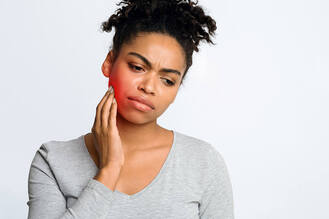 Woman touching her jaw with visible redness, showing pain and discomfort that may require a tooth extraction.